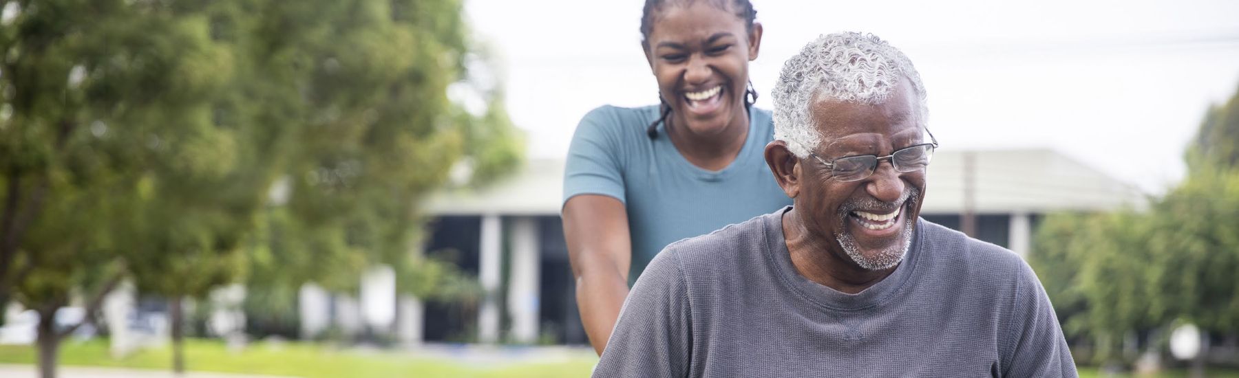A caregiver walking outdoors with an older man, both smiling.
